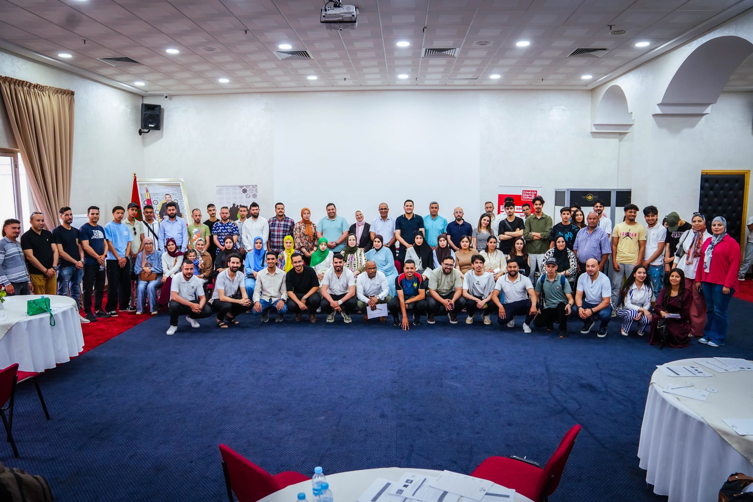IMG-20260524-WA0161 | MCG24 | موقع إلكتروني مغربي شامل متجدد على مدار الساعة Large group of men and women posing for a group photo in a conference room, with curtains, tables, and decorative arches visible in the background.