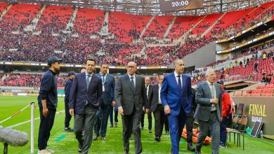 IMG-20260524-WA0216 | MCG24 | موقع إلكتروني مغربي شامل متجدد على مدار الساعة Group of men in suits walking along a soccer field in a large stadium with red seats and a digital scoreboard overhead; crowd seated in the stands behind them.