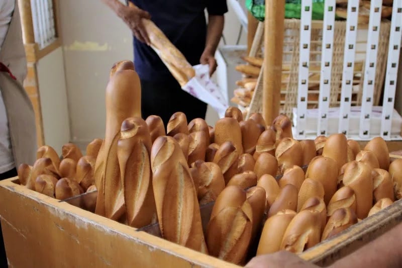 IMG-20260529-WA0056 | MCG24 | موقع إلكتروني مغربي شامل متجدد على مدار الساعة Crate overflowing with long French baguettes in a bakery, with people handling bread in the background.