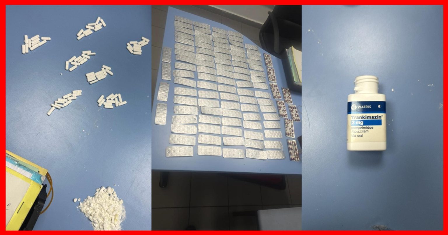 Blue table covered with many white tablets in blister packs arranged in rows; scattered pills and a pile of crushed white powder on the left, and a white bottle labeled Trankimazín 2 mg on the right.