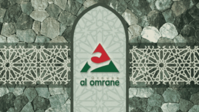 Arched panel on a stone wall displaying the 'al omrane' group logo in red and green. The panel features geometric patterns and is flanked by decorative stone walls.