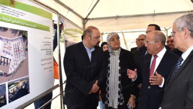 Group of officials in suits examine an architectural display board with Arabic text and photos inside a tent.