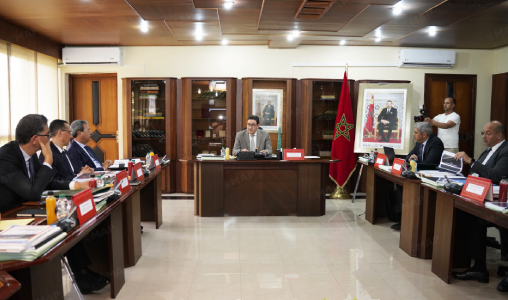 MAP0278965 | MCG24 | موقع إلكتروني مغربي شامل متجدد على مدار الساعة Formal meeting in a conference room with officials seated around two long tables facing a speaker at the head, Moroccan flag nearby.