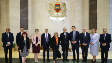 Group of ten people in formal attire posing in a marble lobby with an ornate government crest on the wall behind them.