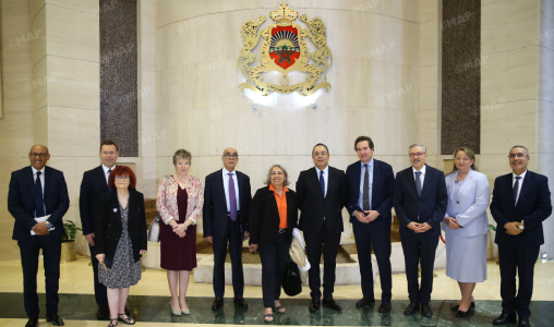 Group of ten people in formal attire posing in a marble lobby with an ornate government crest on the wall behind them.