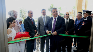 Dignitaries and a young girl participate in a ribbon-cutting opening ceremony as a man in a suit cuts the green ribbon.