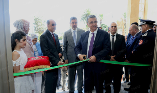 Dignitaries and a young girl participate in a ribbon-cutting opening ceremony as a man in a suit cuts the green ribbon.