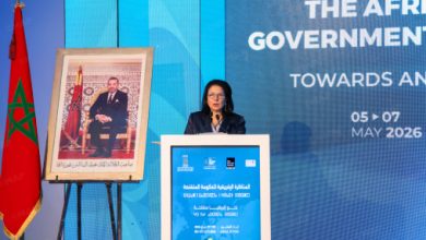 Speaker at a podium during an Africa government conference, with Moroccan flag and a framed portrait beside the stage.