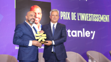 Two men in suits on a stage exchange a gold leaf-shaped trophy at an investment awards ceremony, with a purple backdrop reading 'PRIX DE L'INVESTISSEMENT'.