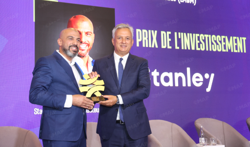 Two men in suits on a stage exchange a gold leaf-shaped trophy at an investment awards ceremony, with a purple backdrop reading 'PRIX DE L'INVESTISSEMENT'.