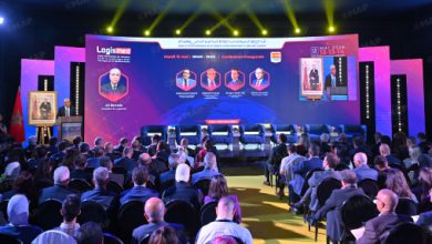 Nouveau-projet15 2 | MCG24 | موقع إلكتروني مغربي شامل متجدد على مدار الساعة Conference hall with a large purple stage screen showing headshots and names of panelists; several panelists seated on stage under yellow spotlights, audience seated and watching.