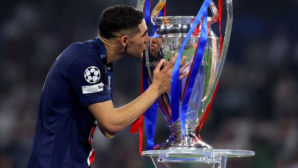 OIHEQP5JFJBCLJMIBYDSJJ5CDU | MCG24 | موقع إلكتروني مغربي شامل متجدد على مدار الساعة Soccer player in a dark blue jersey kisses the UEFA Champions League trophy adorned with blue and red ribbons after a win.