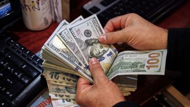 Hands counting a thick stack of U.S. hundred-dollar bills on a desk near a keyboard.