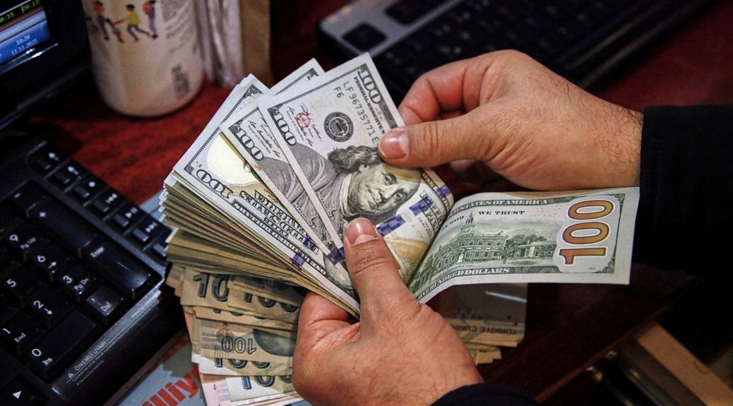 Hands counting a thick stack of U.S. hundred-dollar bills on a desk near a keyboard.