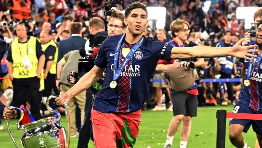 V7MizD49K3_1780173849 | MCG24 | موقع إلكتروني مغربي شامل متجدد على مدار الساعة PSG footballer with medal, arms outstretched, celebrating on the field beside a large trophy. The crowd cheers in the background.
