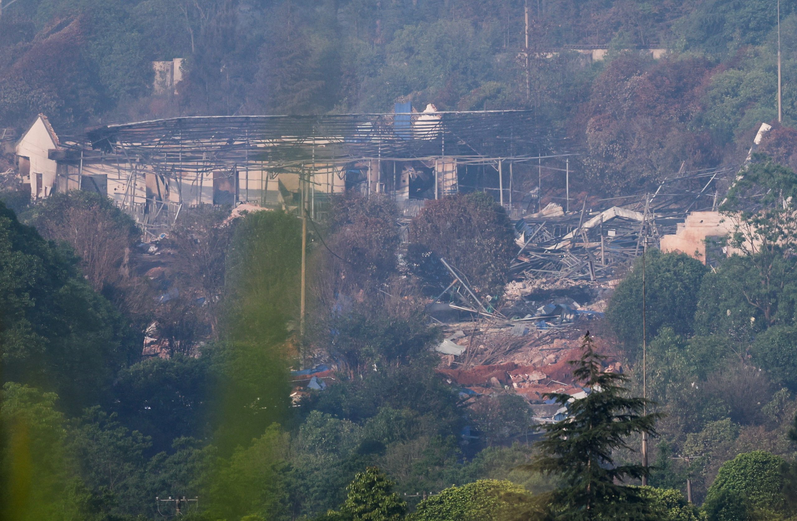 Rubble and the skeletal remains of a collapsed building amid trees, with debris strewn across the area.