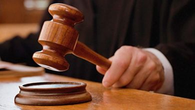 A wooden gavel about to strike a sound block on a courtroom desk