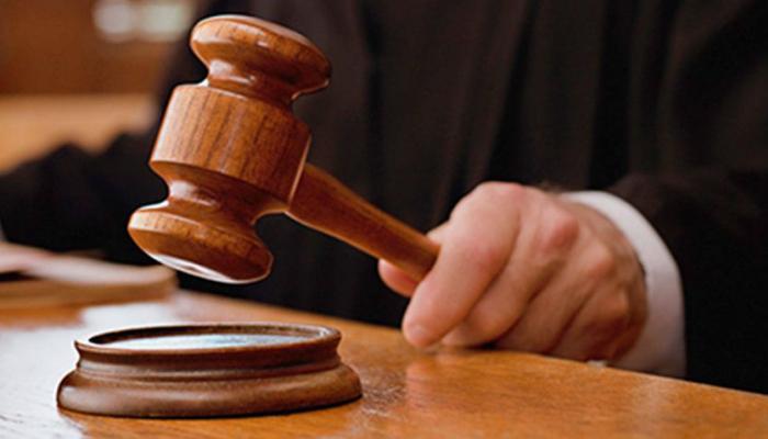A wooden gavel about to strike a sound block on a courtroom desk
