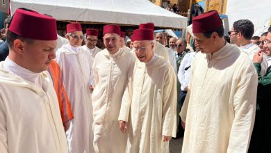 Group of men in white traditional robes and red fezzes at an outdoor ceremony near a white tent.