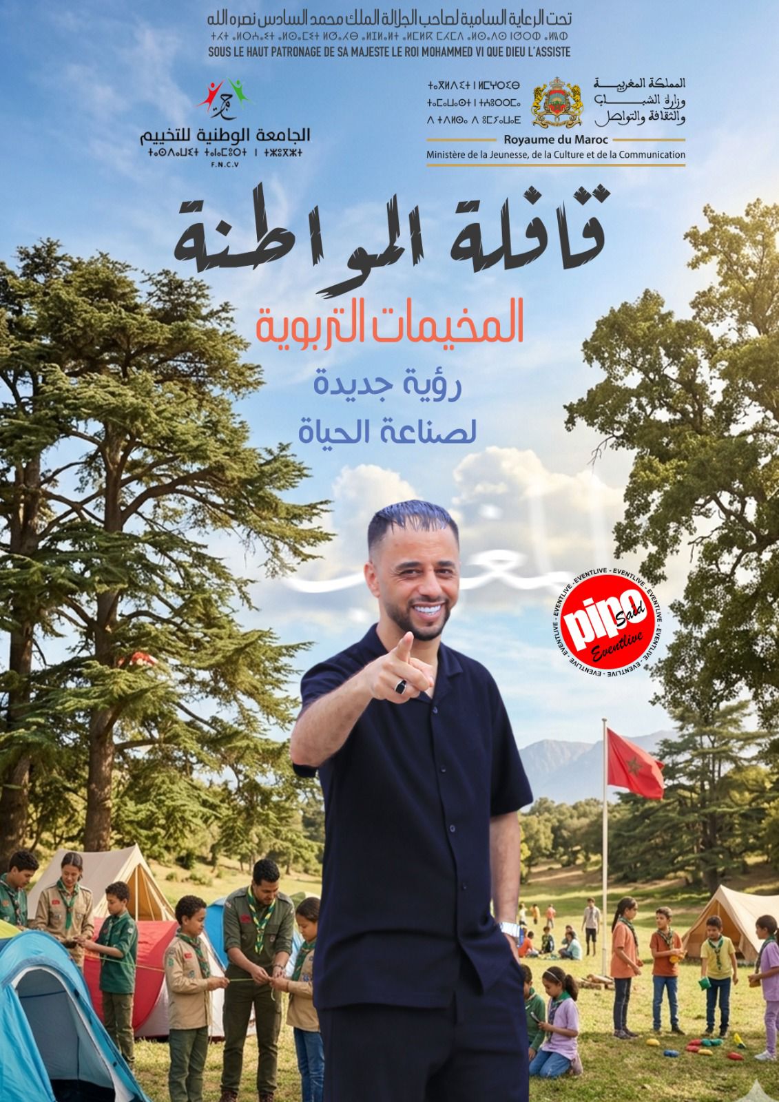 قائد يبتسم وهو يشير إحالة نحو الكاميرا أمام مخيم صيفي مع أطفال وشبان حوله وتُّخيمات في الخلف.