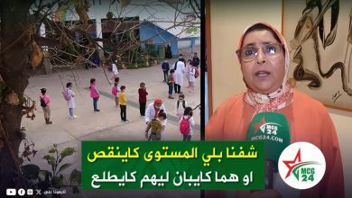 News footage showing schoolchildren lined up outdoors while an interviewer reports from a studio, banner in Arabic text at bottom.