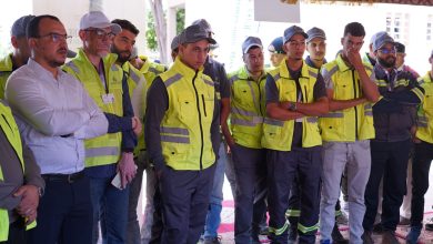 Group of workers in high-visibility yellow vests standing together, listening to a briefing under a decorative canopy.