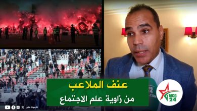 Collage: fans lighting flares, a packed stadium, and a man in a suit being interviewed with a green Arabic banner in the foreground.