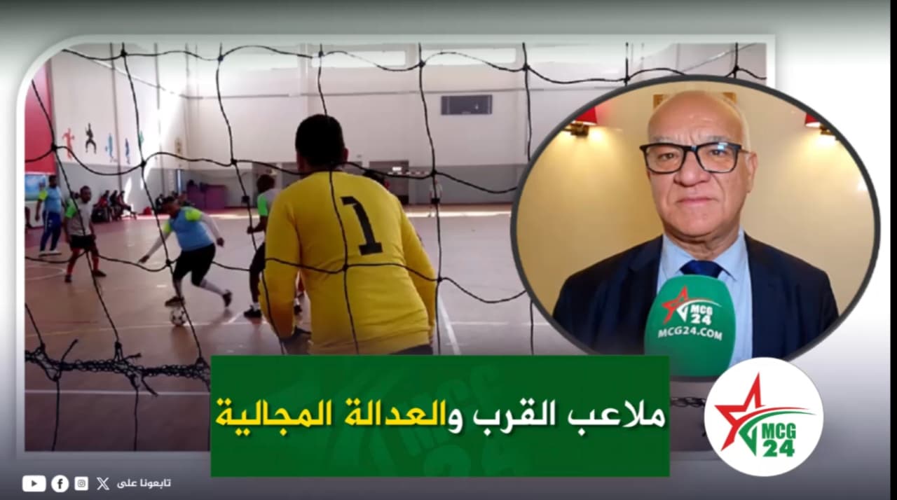 News thumbnail showing an indoor futsal match with a yellow-jersey goalkeeper (#1) and players, plus a circular inset of a man in a suit giving an interview with a green microphone. Arabic headline bar at bottom.