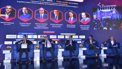 WhatsApp Image 2026-05-14 at 101955 | MCG24 | موقع إلكتروني مغربي شامل متجدد على مدار الساعة Panel of five men in suits seated on a blue stage during a formal conference, with a large backdrop of portraits and event text behind them.