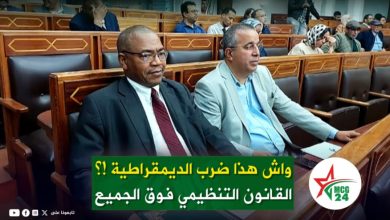 WhatsApp Image 2026-05-16 at 172234 | MCG24 | موقع إلكتروني مغربي شامل متجدد على مدار الساعة Two men in business attire sit in a formal assembly hall; an Arabic news banner runs across the bottom and a round logo appears at the bottom-right.
