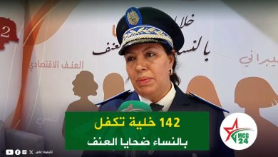 Police spokeswoman in uniform speaking at a press conference, microphone in front, Arabic backdrop and MCG 24 logo.