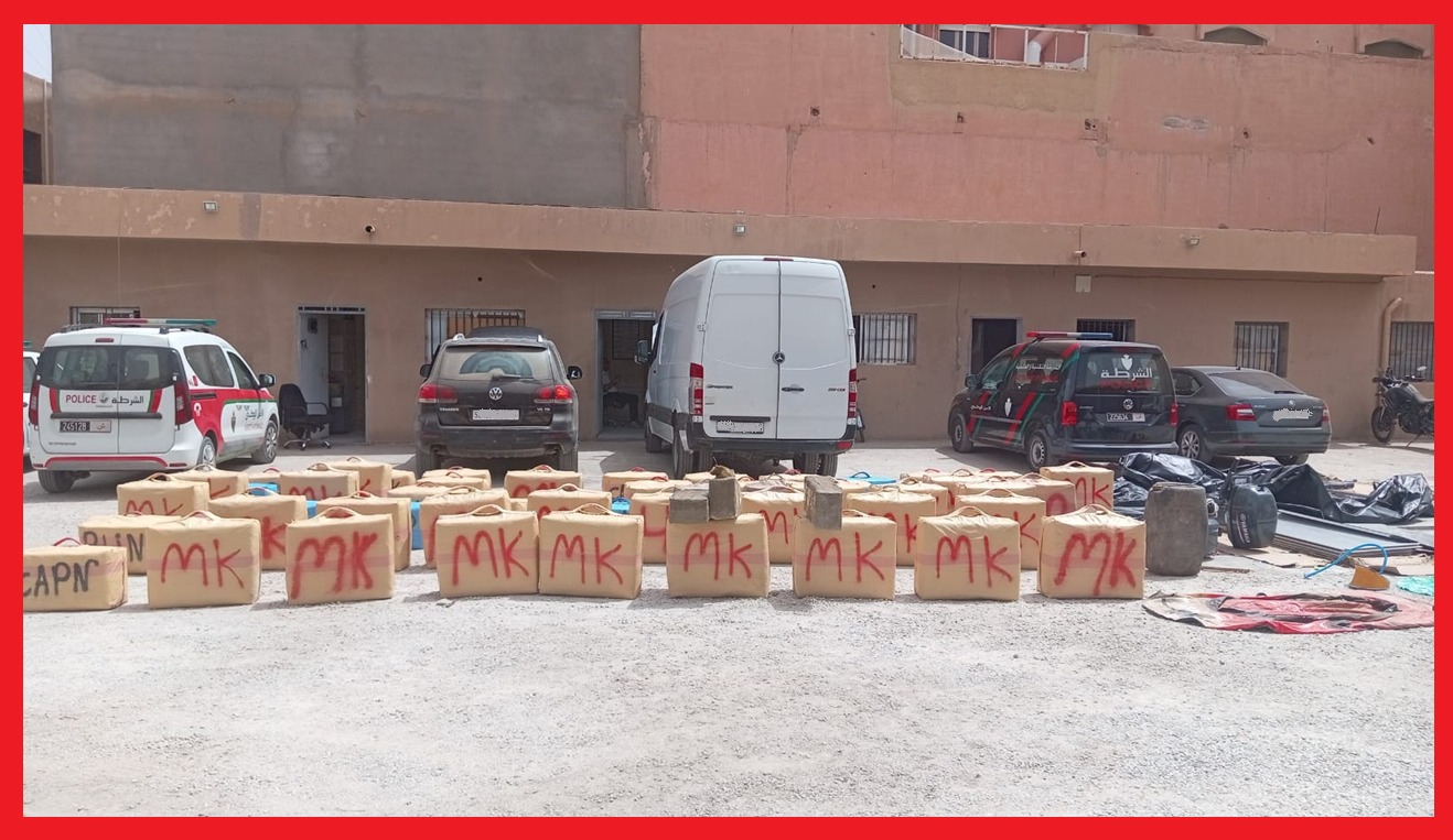 Row of tan bundles labeled MK lined up on a gravel lot with police cars and a white van in the background.