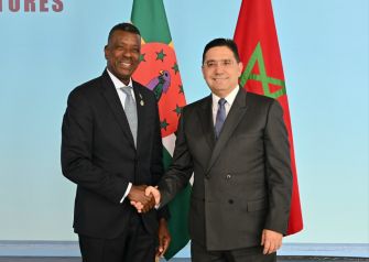 WhatsApp Image 2026-05-21 at 144251 | MCG24 | موقع إلكتروني مغربي شامل متجدد على مدار الساعة Two men in dark suits shake hands in front of a blue backdrop with flags behind them, signaling a formal meeting or agreement.