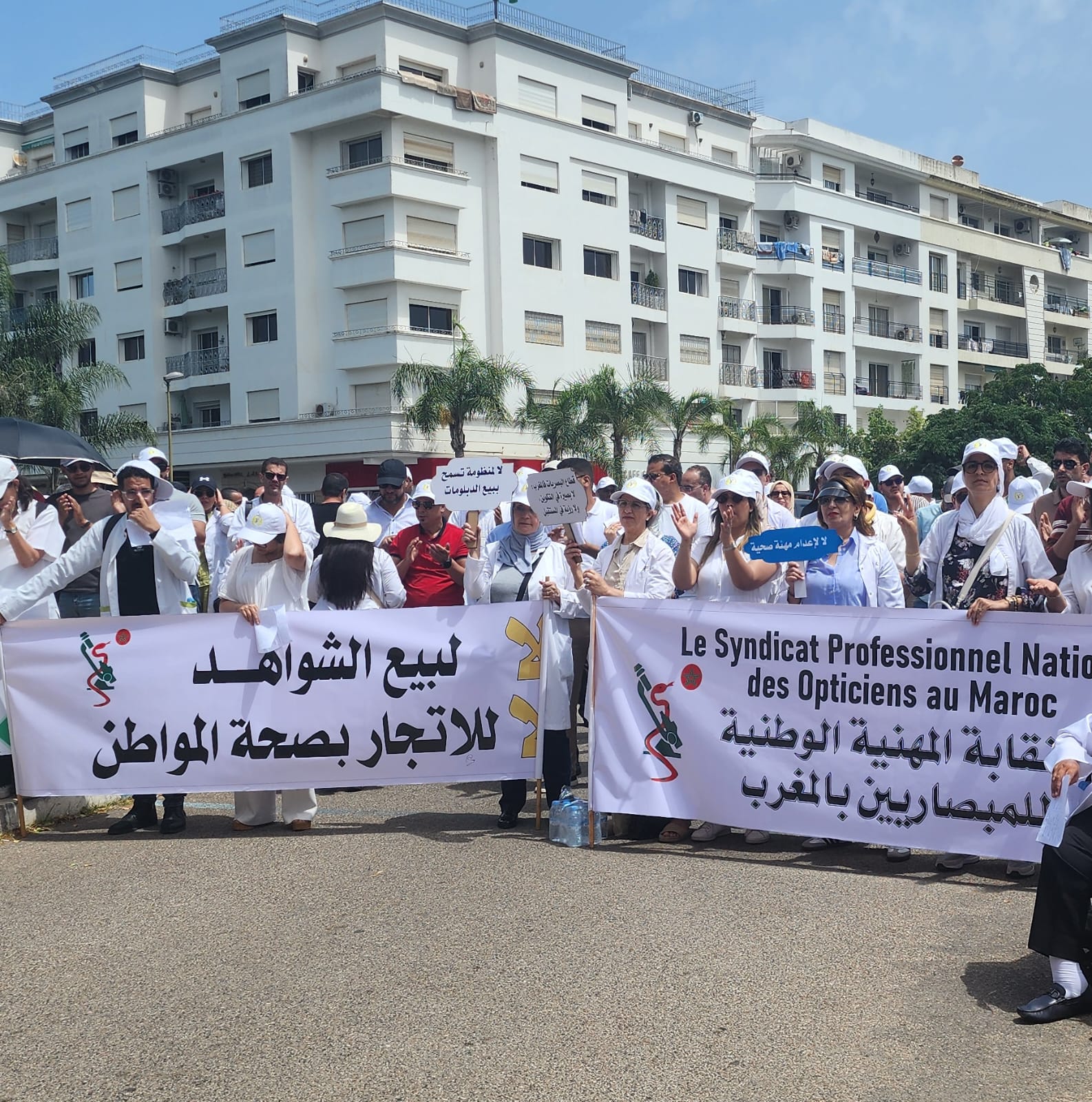WhatsApp Image 2026-05-25 at 112804 | MCG24 | موقع إلكتروني مغربي شامل متجدد على مدار الساعة Group of protesters in white clothing holding large banners with Arabic and French text, in front of a white apartment building.