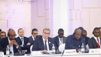 A group of officials in suits seated at a long conference table with microphones and nameplates, including a Morocco sign in front of one speaker.