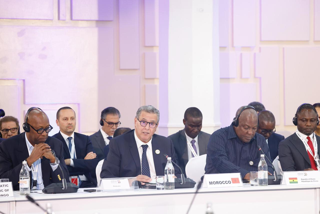 A group of officials in suits seated at a long conference table with microphones and nameplates, including a Morocco sign in front of one speaker.