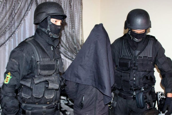 bcij | MCG24 | موقع إلكتروني مغربي شامل متجدد على مدار الساعة Two masked armed security personnel escort a person in a dark hooded cloak.
