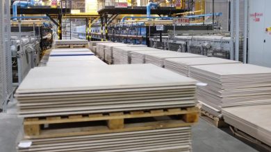 ceramique-APIC | MCG24 | موقع إلكتروني مغربي شامل متجدد على مدار الساعة Industrial plywood sheets stacked on pallets in a manufacturing facility with machinery in the background.