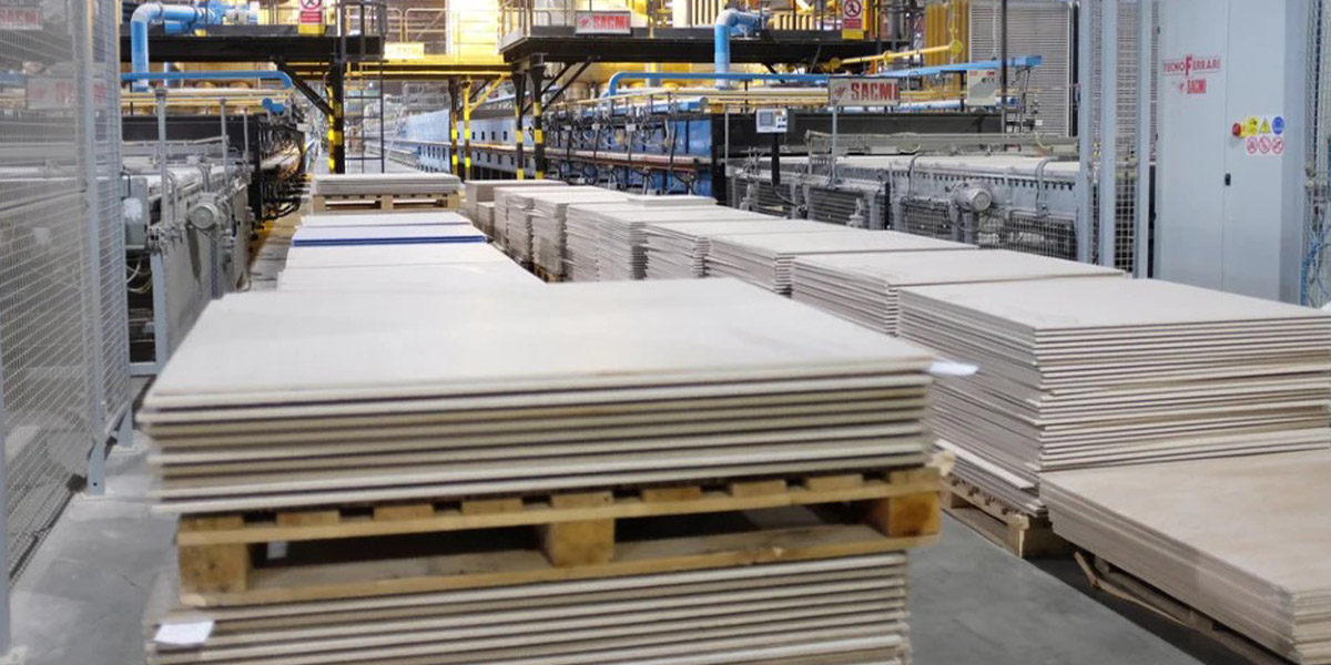 ceramique-APIC | MCG24 | موقع إلكتروني مغربي شامل متجدد على مدار الساعة Industrial plywood sheets stacked on pallets in a manufacturing facility with machinery in the background.