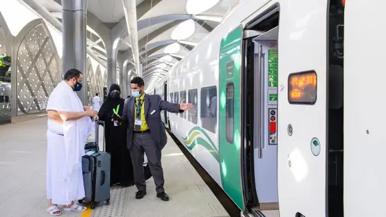 Passengers wearing masks stand on a platform as a white-green train doors open for boarding.