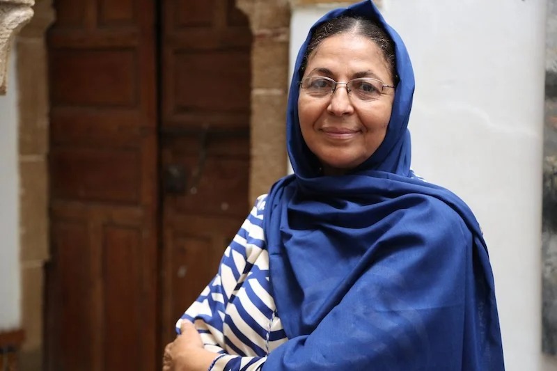 fadila-benmoussa1 | MCG24 | موقع إلكتروني مغربي شامل متجدد على مدار الساعة Woman wearing a blue hijab and striped shirt stands outdoors, smiling at the camera.