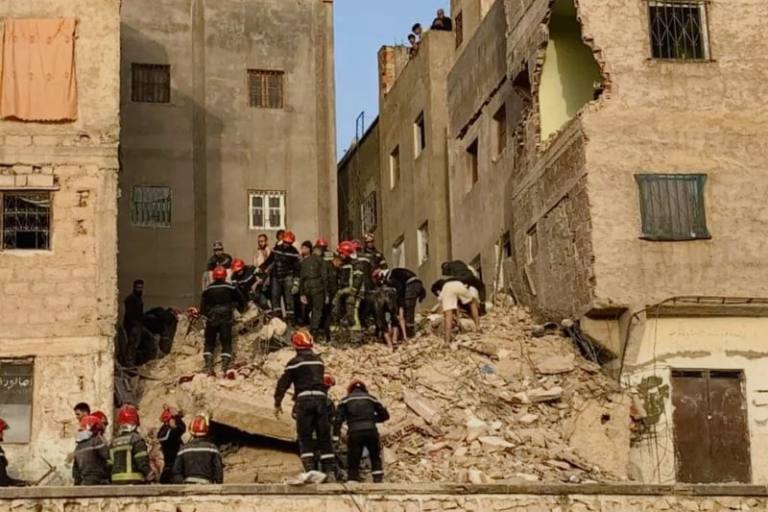 fes-effondrement-768x512 | MCG24 | موقع إلكتروني مغربي شامل متجدد على مدار الساعة Emergency responders in orange helmets search through a collapsed building's rubble between beige apartment blocks, with onlookers atop the walls.