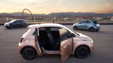 123 | MCG24 | موقع إلكتروني مغربي شامل متجدد على مدار الساعة Pink compact car with open doors in the foreground on a rooftop parking lot at sunset, two small cars in the background and a cityscape beyond.