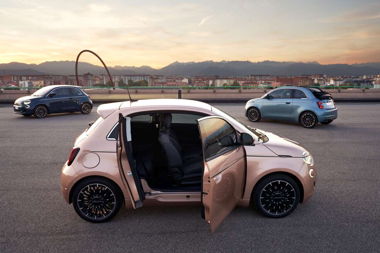 123 | MCG24 | موقع إلكتروني مغربي شامل متجدد على مدار الساعة Pink compact car with open doors in the foreground on a rooftop parking lot at sunset, two small cars in the background and a cityscape beyond.