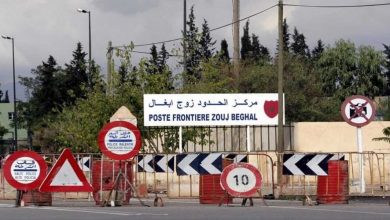 Border crossing with multiple construction barriers and traffic signs, including a 10 km/h speed sign and no-entry/stop signs, under a sign reading 'Poste Frontière Zouj Beghal' in Arabic and French.