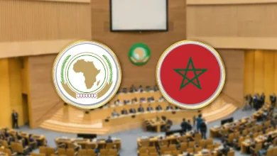 Formal international meeting in a chamber; two large round emblems above delegates: Africa Union on the left and Morocco flag on the right.