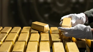 Gloved hands stacking gold bars in a secure vault or storage area.