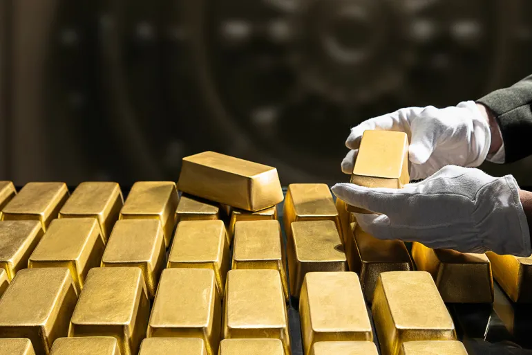 Gloved hands stacking gold bars in a secure vault or storage area.