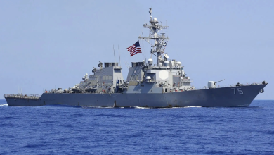 Gray U.S. Navy destroyer sailing on calm blue sea with an American flag flying from the mast.