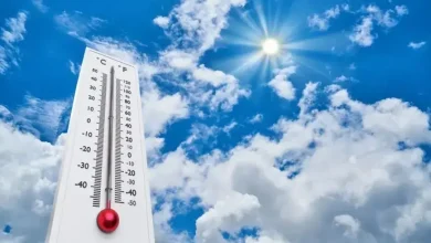 Outdoor thermometer against a bright blue sky with sun, indicating hot weather